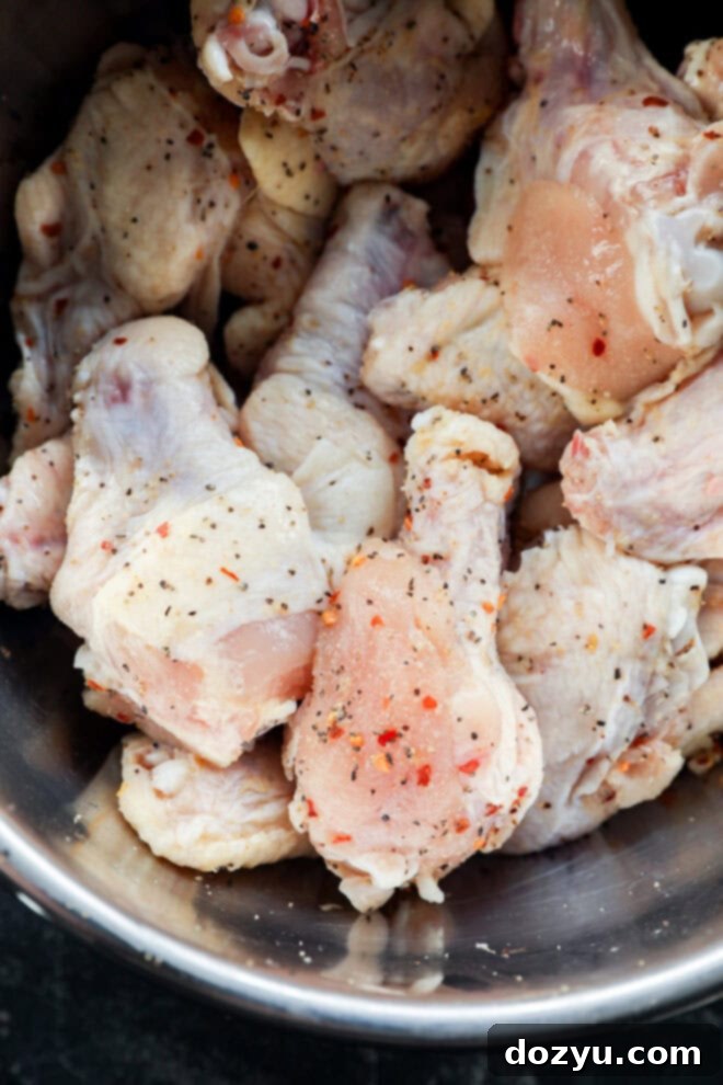 Sweet and Sticky Honey Garlic Chicken Wings 4 A close-up of raw chicken drumsticks and wings in a metal bowl, seasoned with black pepper and red chili flakes.