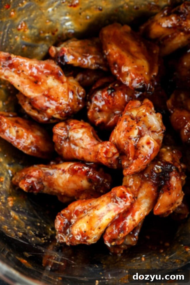 Sweet and Sticky Honey Garlic Chicken Wings 7 A close-up of glazed honey garlic chicken wings coated in a sticky, reddish-brown sauce with visible seasoning, piled together in a glass bowl.