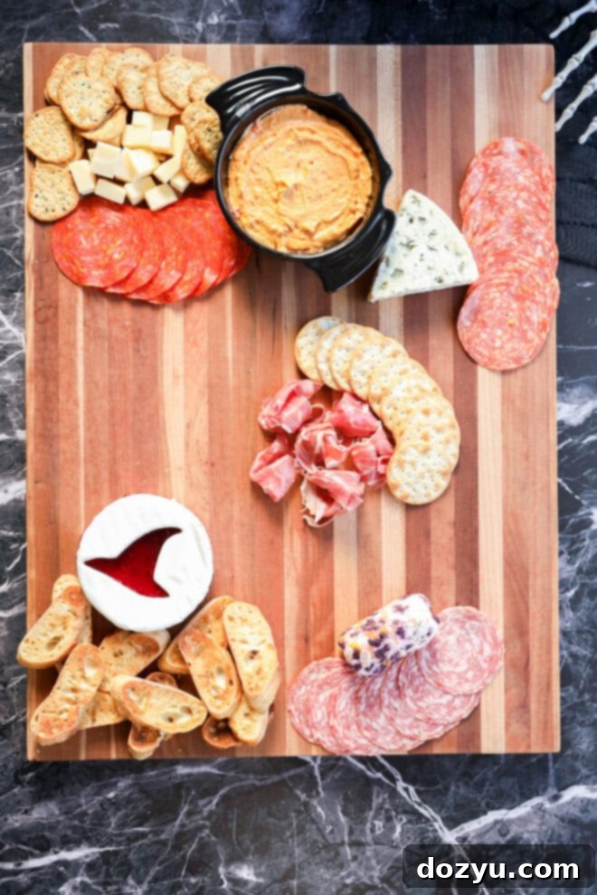 Featuring assorted crackers, cheese cubes, sliced salami, pepperoni, blue cheese, prosciutto, a brie round with jam, a cheese log, crostini, and a bowl of orange dip—perfect for spooky celebrations.