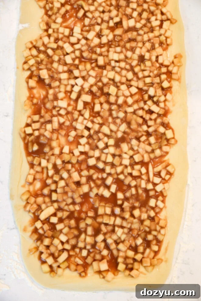 Dough rolled out flat and topped with a mixture of small diced apples and cinnamon filling, just like Apple Pie Filled Cinnamon Rolls, ready to be rolled or baked.