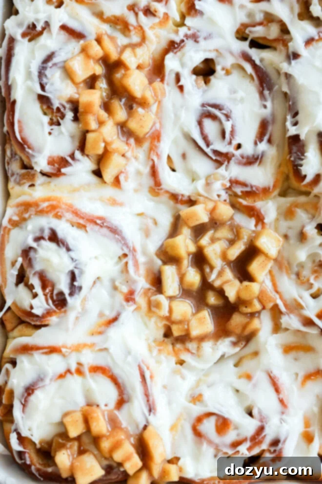 Close-up of Apple Pie Filled Cinnamon Rolls topped with creamy white frosting and diced cooked apples in cinnamon sauce, creating a gooey and appealing texture.