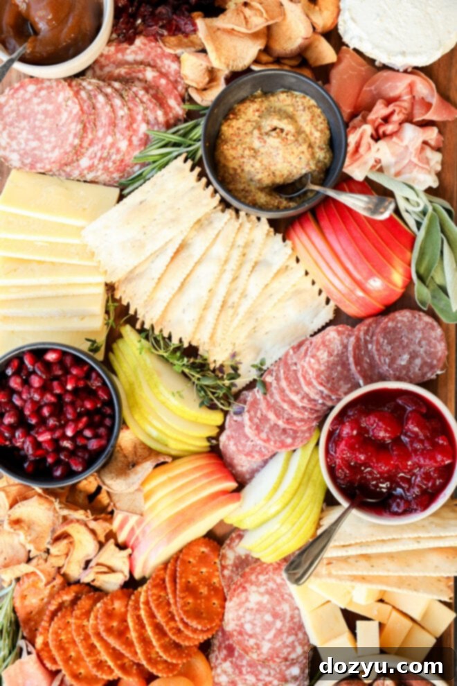 A vibrant Thanksgiving charcuterie board featuring sliced meats, an assortment of cheeses, crackers, apple and pear slices, pomegranate seeds, mustards, fruit preserves, chips, and herbs—beautifully arranged for your holiday celebration.