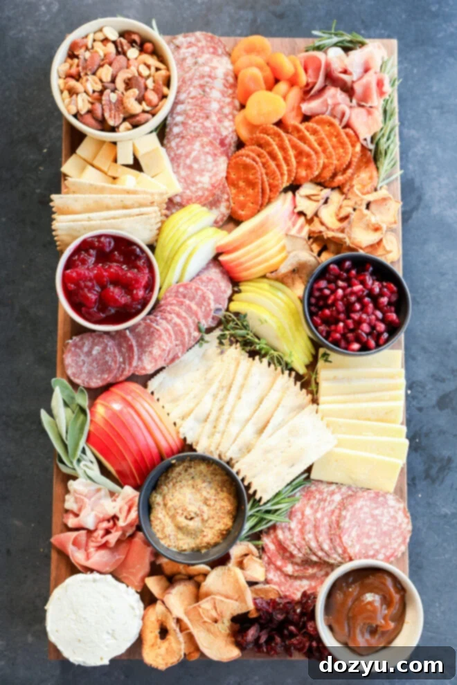 A Thanksgiving charcuterie board with cheeses, sliced meats, crackers, dried fruits, apple slices, nuts, bowls of mustard, cranberry sauce, pomegranate seeds, and caramel dip.