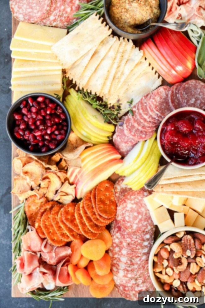 A Thanksgiving charcuterie board with salami, prosciutto, crackers, cheeses, apple and pear slices, dried apricots, nuts, pomegranate seeds, dried fruit chips, mustard, cranberry sauce, and herb garnishes.