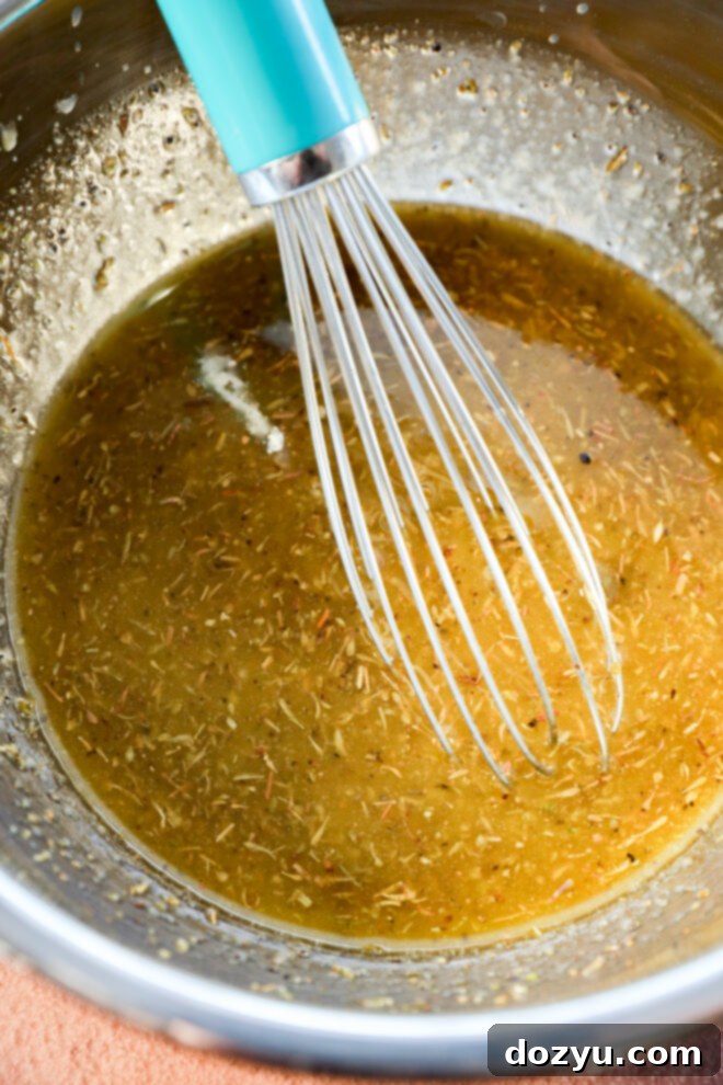 Lemon Herb Roasted Chicken and Potatoes 4 A metal bowl containing a yellow-brown herb marinade with a whisk that has a turquoise handle.