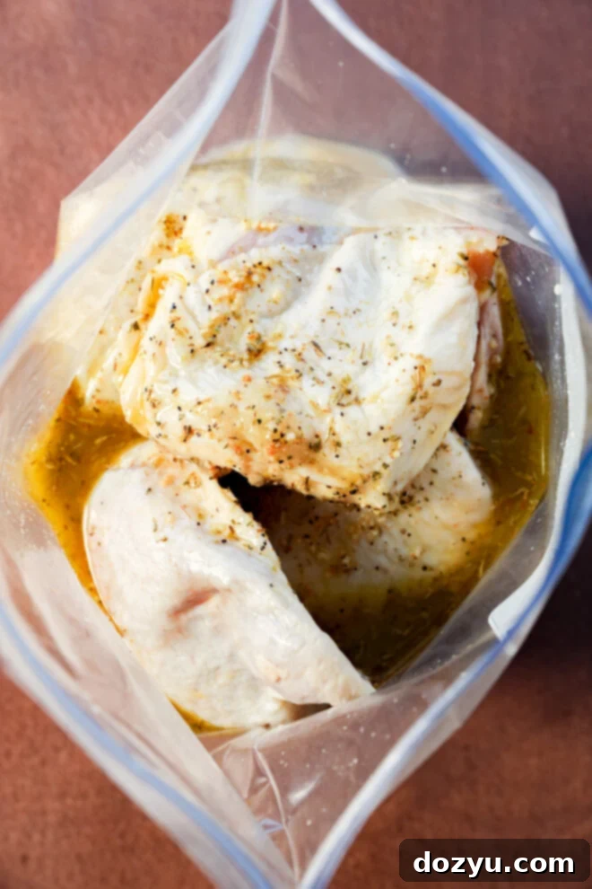 Lemon Herb Roasted Chicken and Potatoes 5 Raw chicken pieces marinating in a clear plastic zip-top bag with an herb marinade