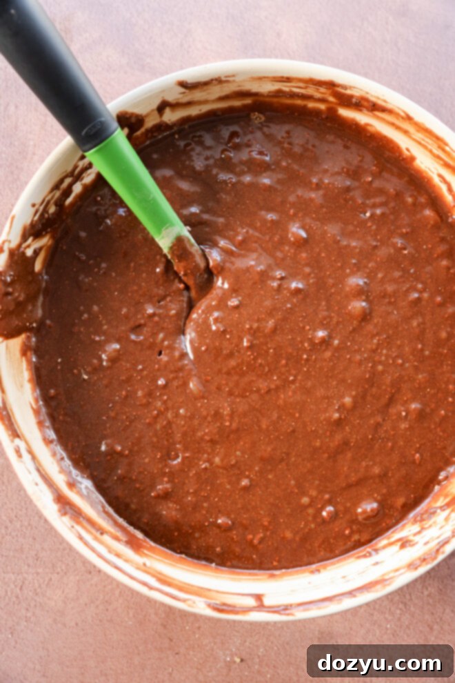 Brownie cake batter being mixed with a green spatula.