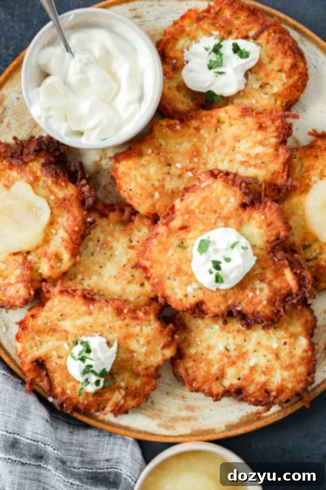 A plate of golden, crispy Jewish latkes topped with sour cream and chopped herbs, served with bowls of sour cream and applesauce on the side.
