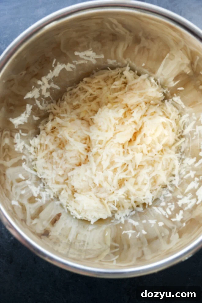 Freshly grated russet potatoes in a stainless steel bowl.