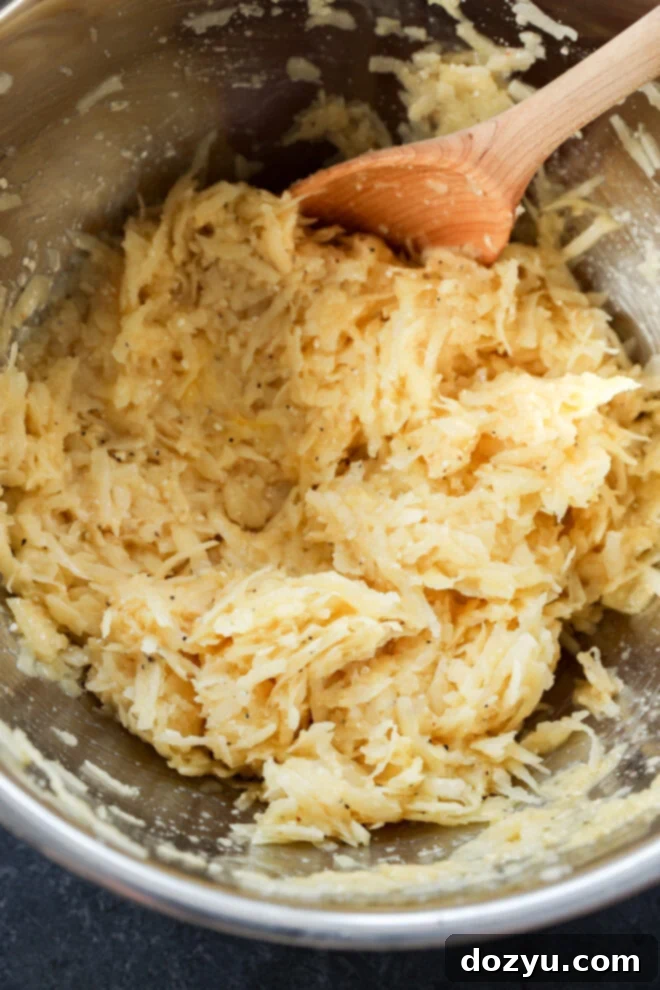 A metal bowl containing a mixture of grated potatoes and seasonings.